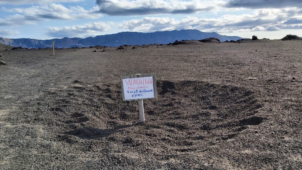 The ground has sunk and there is a visibile pit. Warning sign say "melting permafrost".